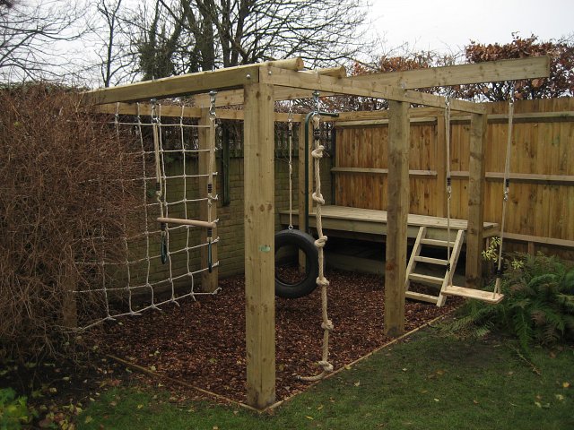 Children's playframe with play bark, swing, knotted rope, climbing net, swinging tyre, trapese and platform
